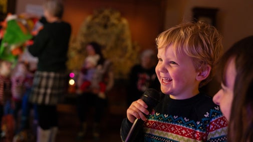 A little boy grins as he holds a microphone next to his family, singing karaoke in the State Bedroom at Lyme.